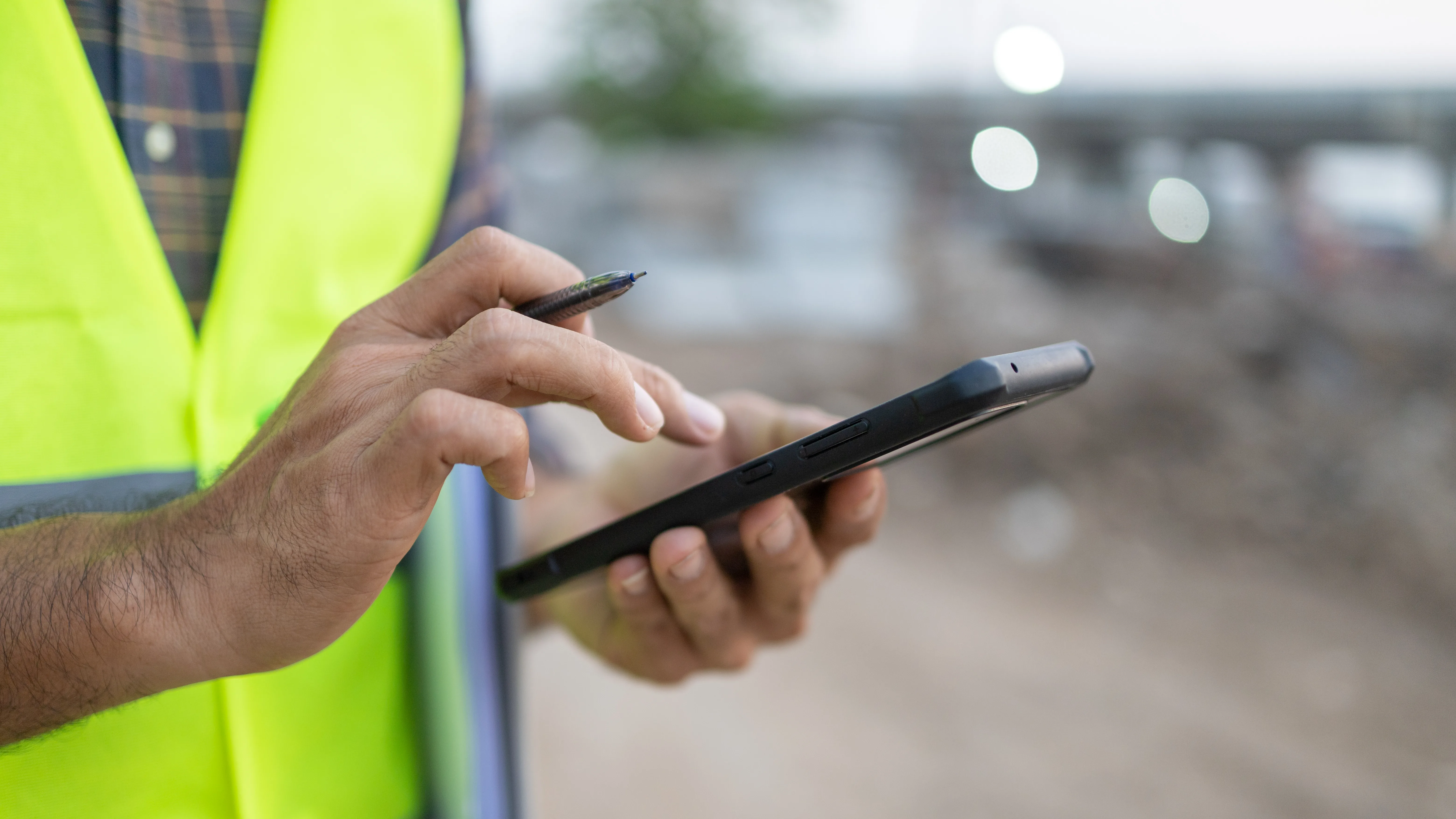 Uomo in cantiere che scrive su uno smartphone