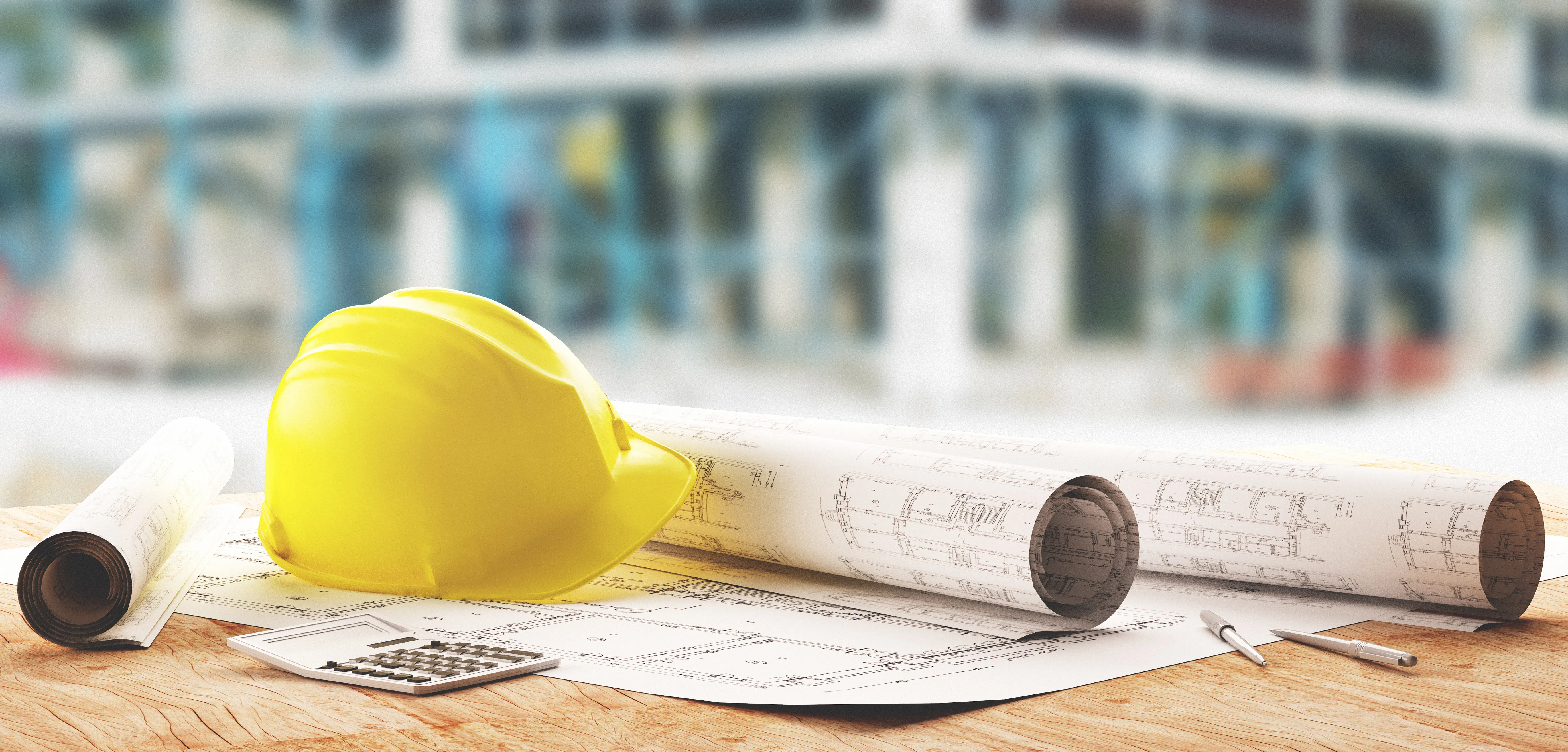 Tavolo con un elmetto da cantiere e fogli con disegni tecnici