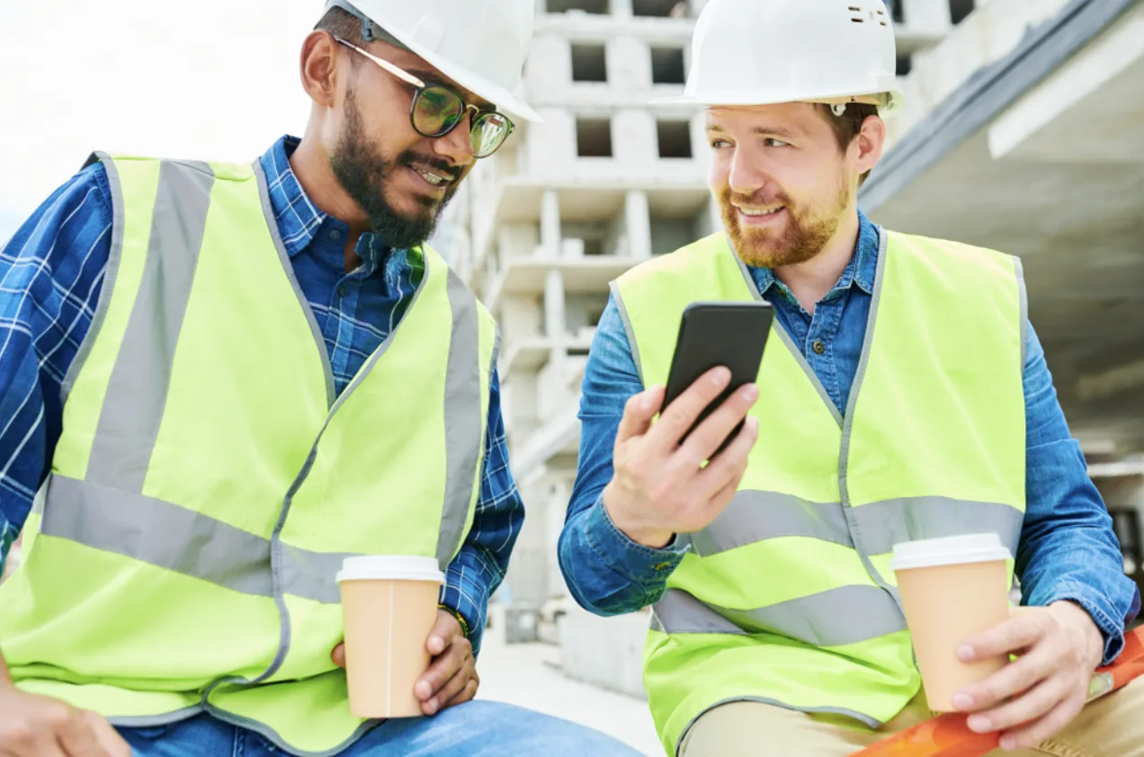 Due uomini in cantiere osservano uno smartphone