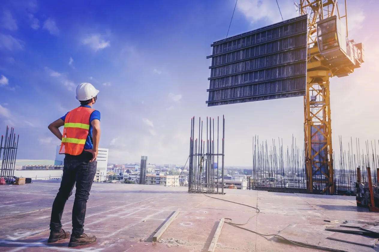 Uomo di spalle in cantiere che osserva una gru che posa una lastra